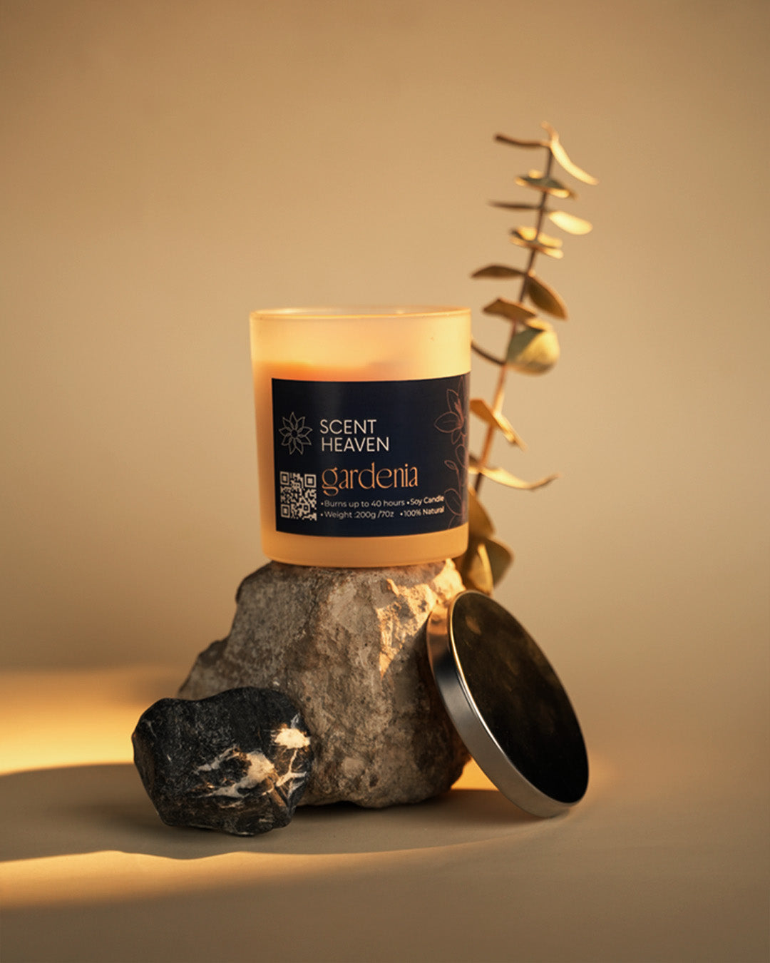 Candle with 'Scent of Heaven' label on a rock with a plant, on a warm beige background